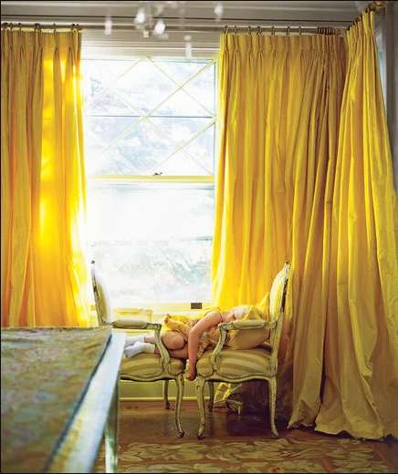 小女孩睡在雙併華麗單人椅上，就在金黃色落地窗簾之前